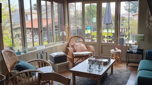 Un salón acogedor con muebles de mimbre, un sofá verde y vistas al patio trasero a través de amplios ventanales.