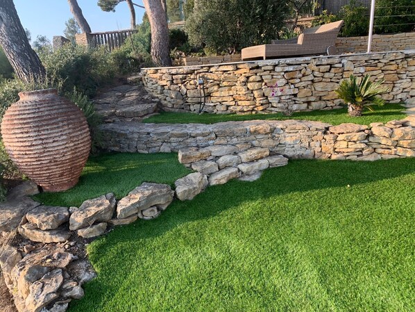 A landscaped garden with a stone retaining wall, a large decorative pot, and a grassy area.