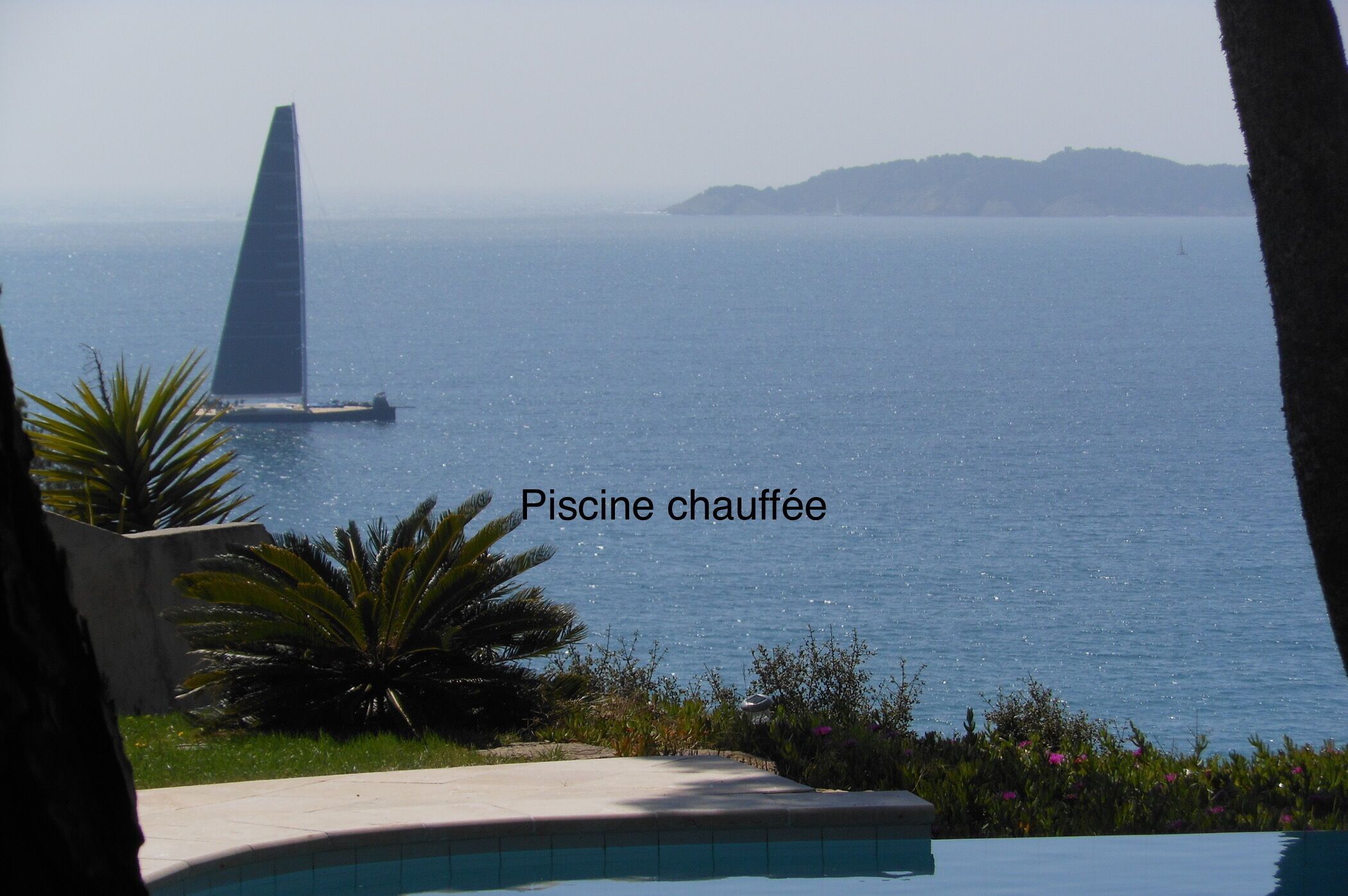 Una piscina con vistas al mar y un velero en la distancia.