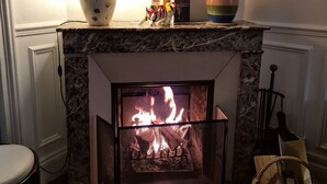 Een haard met een vlam, een lamp, een decoratief bord en een klein beeldje op de schoorsteenmantel.
