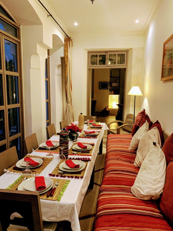 A dining area with a long table set for a meal, a sofa with pillows, and a lamp.