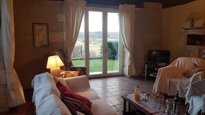 A living room with a sofa, a table with drinks, a TV, and a view through large windows. - Country house, quiet location, private pool. Country house. Magnificent view. (Montcuq en Quercy Blanc)