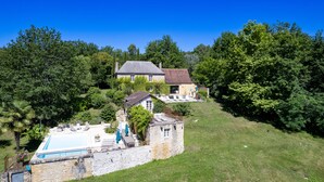 A large house with a swimming pool, surrounded by lush greenery and trees.