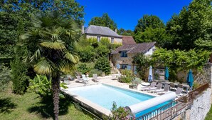 A stone house with a swimming pool, surrounded by lush greenery and trees.