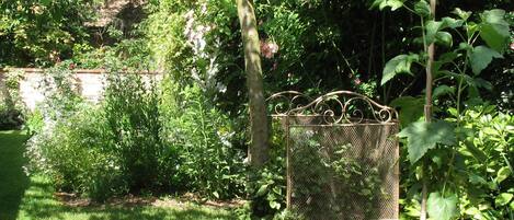 Een tuin met een metalen vogelvoerder, weelderig groen en een bakstenen muur op de achtergrond.