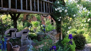 Un jardin agrémenté d’une terrasse en bois, de fauteuils en osier, de plantes en pot et d’un mur en briques.