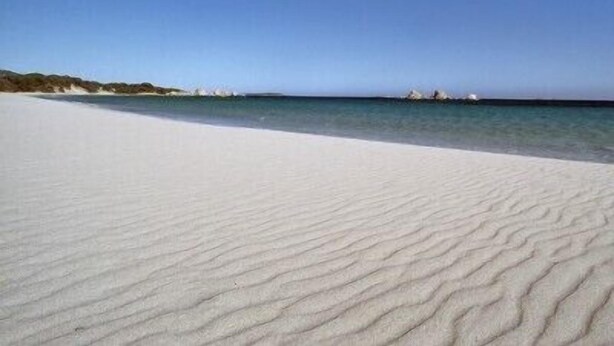 Una spiaggia con sabbia bianca e acqua calma.