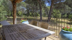 Un tavolo e sedie di legno su un patio esterno con ringhiera metallica, circondato da alberi.