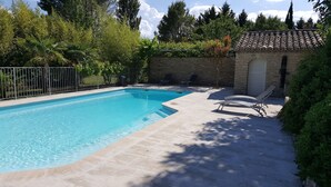 En rektangulær swimmingpool med en stenvæg og et flis tag i baggrunden.