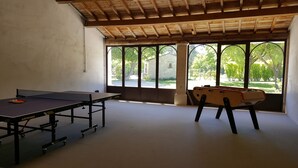 Et rum med et ping pong-bord, et bordfodboldbord og store vinduer med udsigt til grøn natur.