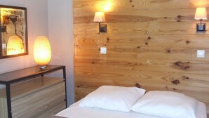 A bedroom with a wooden headboard, two bedside lamps, a nightstand with a lamp, and a painting on the wall. - Vaujany, alpes d'huez, ski, bike, hike, trail chalet 40m2 2/5p, (Vaujany)