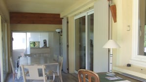 A dining area with a wooden table and chairs, a lamp, and a view of a kitchen and outdoor area. - Vaujany, alpes d'huez, ski, bike, hike, trail chalet 40m2 2/5p, (Vaujany)