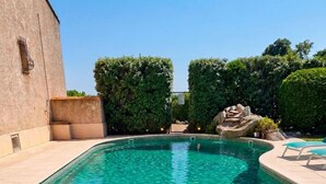 Una piscina rectangular con agua azul cristalina, rodeada por una solana con baldosas y muros de piedra.