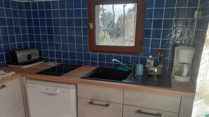 Una cocina con azulejos azules, una ventana, un lavabo, una cafetera y un lavavajillas.