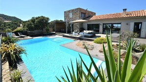 A modern house with a swimming pool, outdoor seating, and a stone facade.