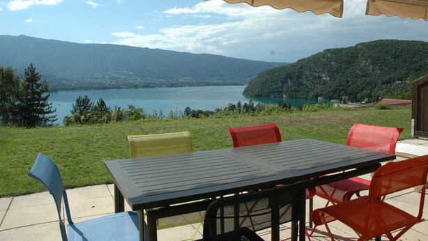 An outdoor patio with a table and chairs, overlooking a lake and mountains.