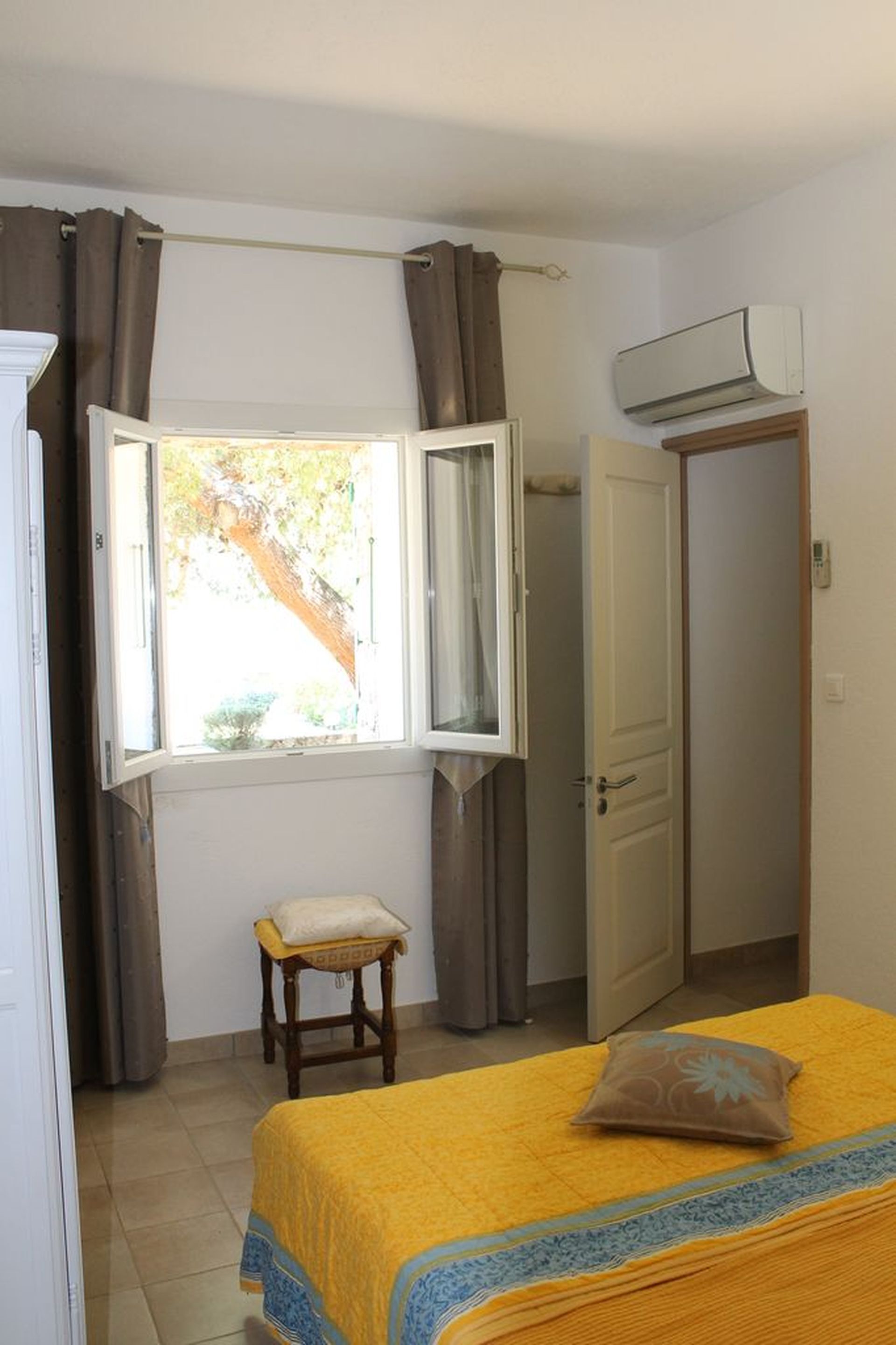 Ein Schlafzimmer mit einem Bett, einem Fenster mit Vorhängen, einer Klimaanlage und einer Tür.