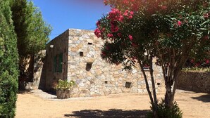 Edifici de pedra amb un petit jardí, un camí pavimentat i un cel blau clar.