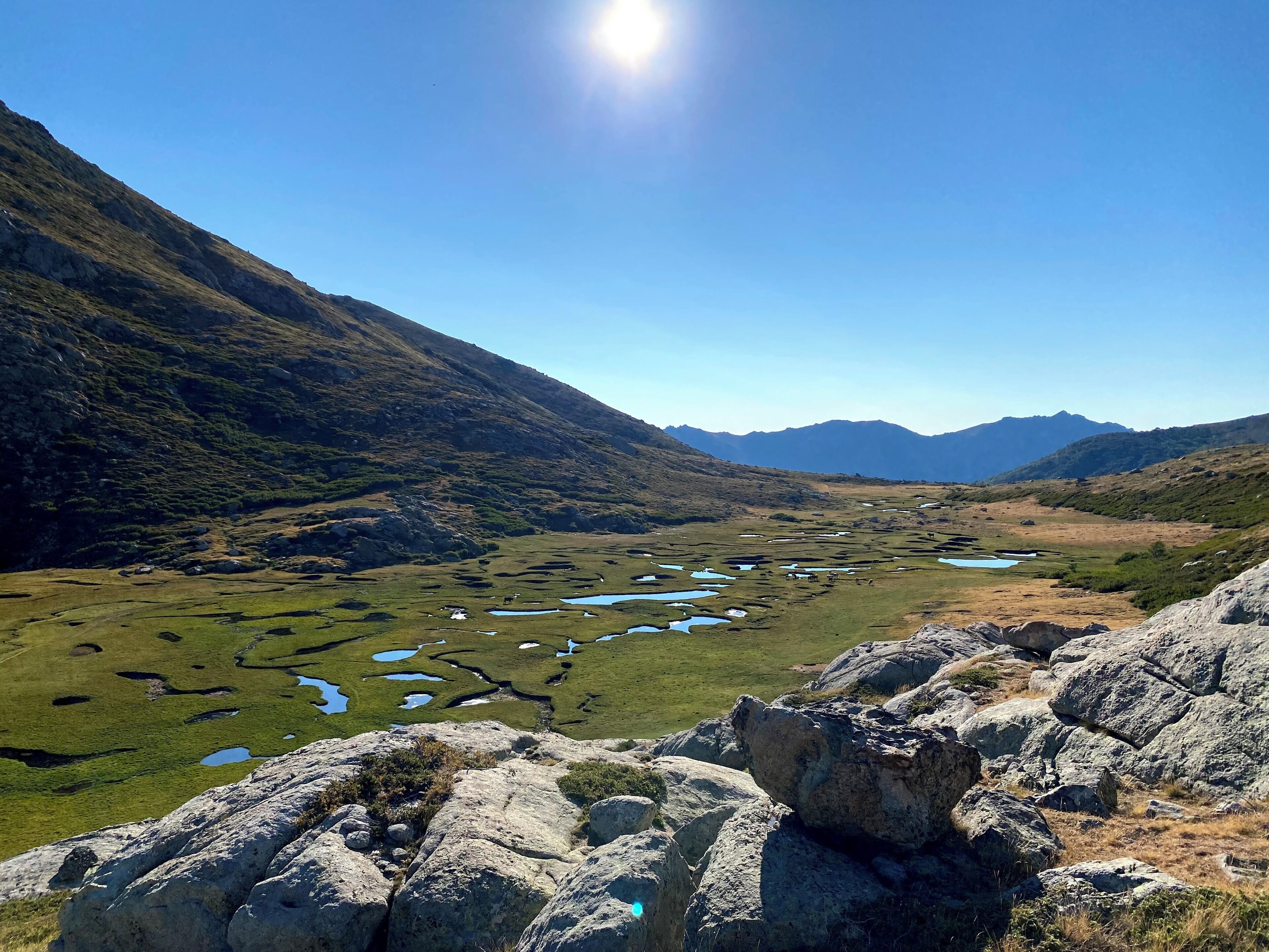 Un paisaje montañoso con un valle, primer plano rocoso y montañas distantes bajo un cielo despejado.