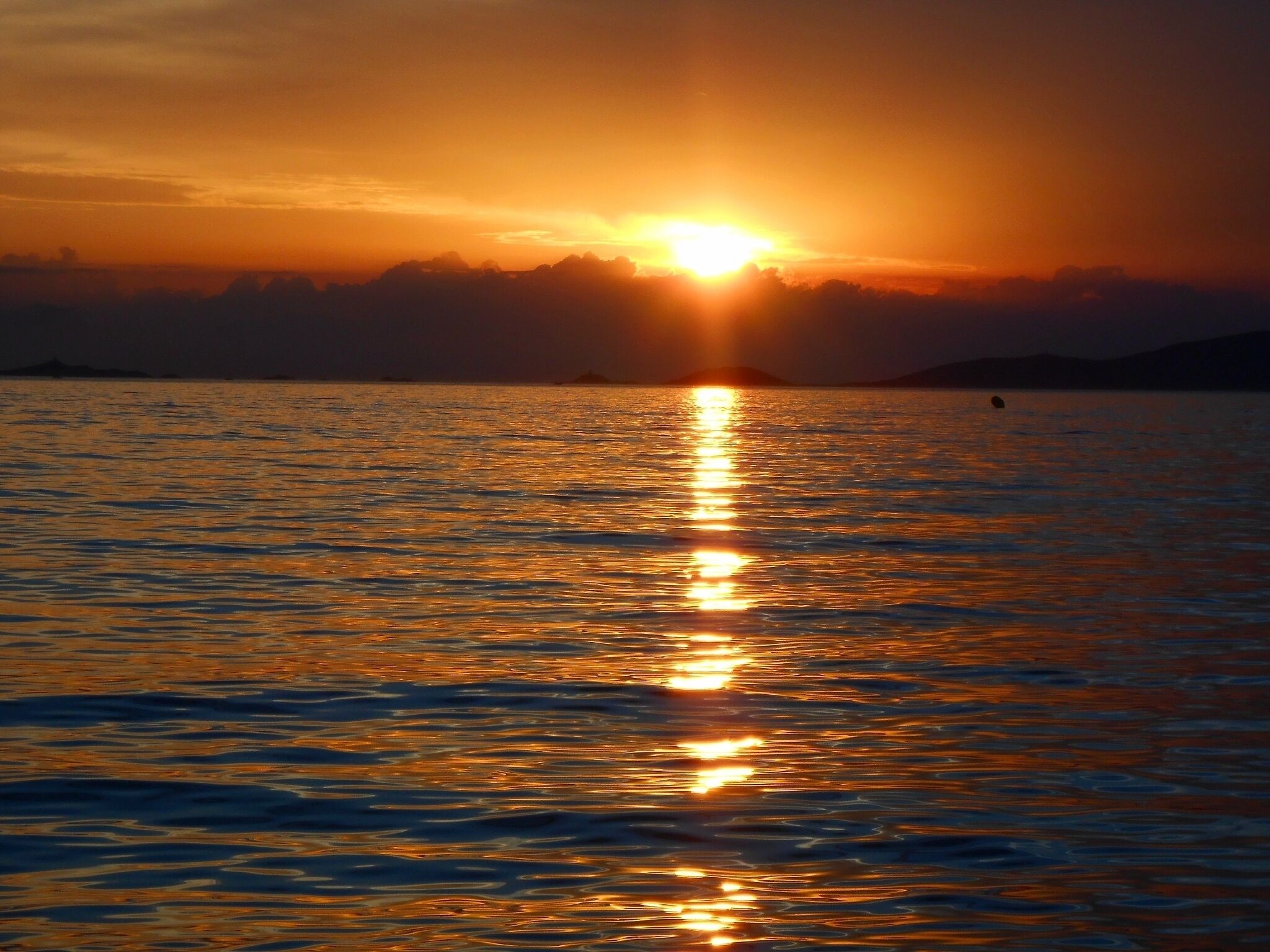 Un coucher de soleil sur une mer calme, le soleil se reflétant sur l’eau.
