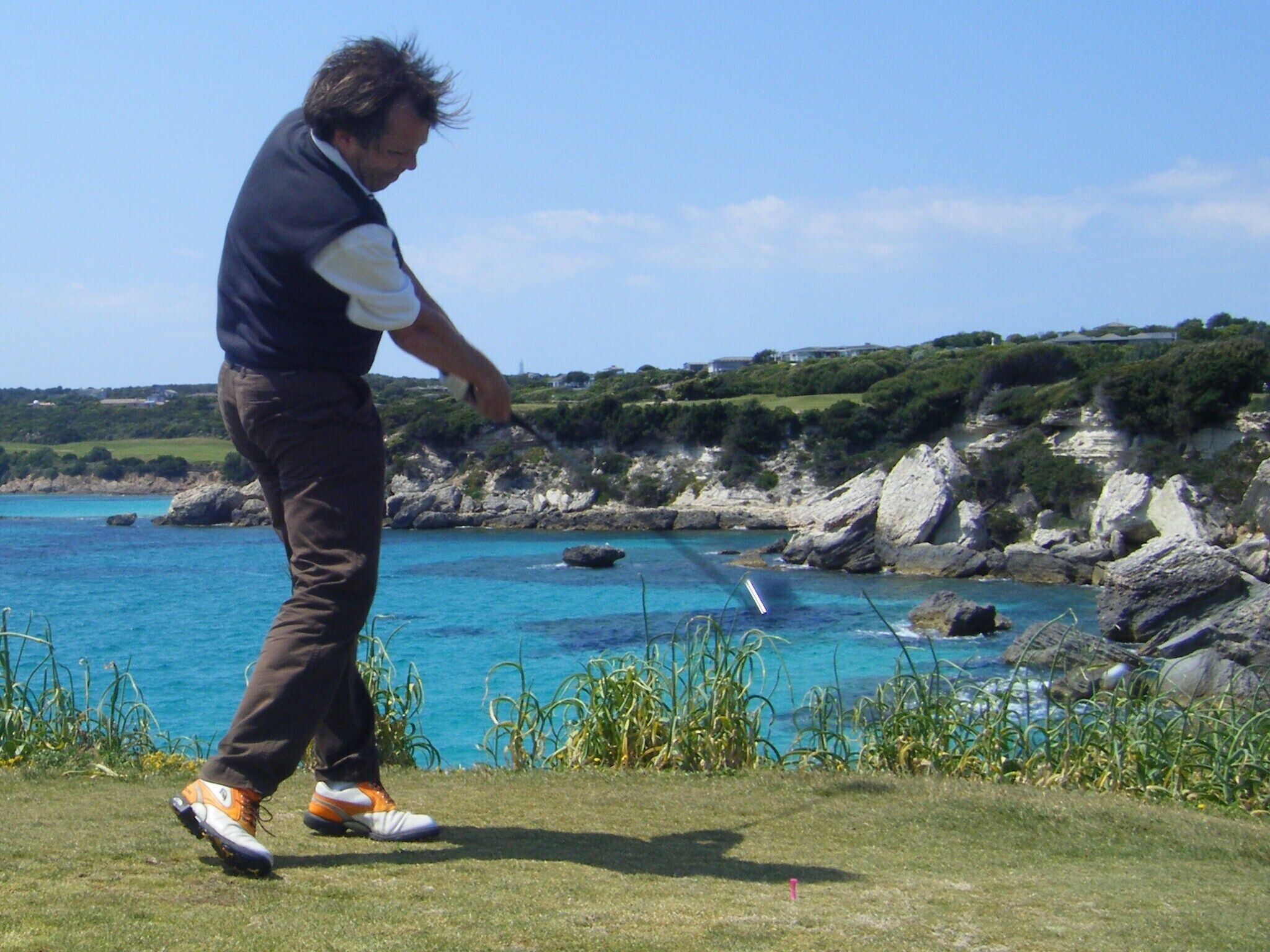 A person playing golf on a grassy area with a coastal view.