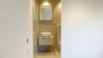Een moderne badkamer met een witte wastafel, een spiegel erboven en beige tegels op de wanden en vloer.