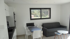 Una cocina moderna con armarios blancos, una mesa de comedor con sillas, un sofá gris y una pequeña mesa blanca con una revista.