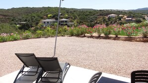Una zona de estar al aire libre cubierta con dos sillones reclinables, suelo de grava y vistas a casas y vegetación al fondo.