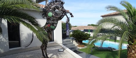 A modern house with a swimming pool, palm trees, and a unique sculpture.