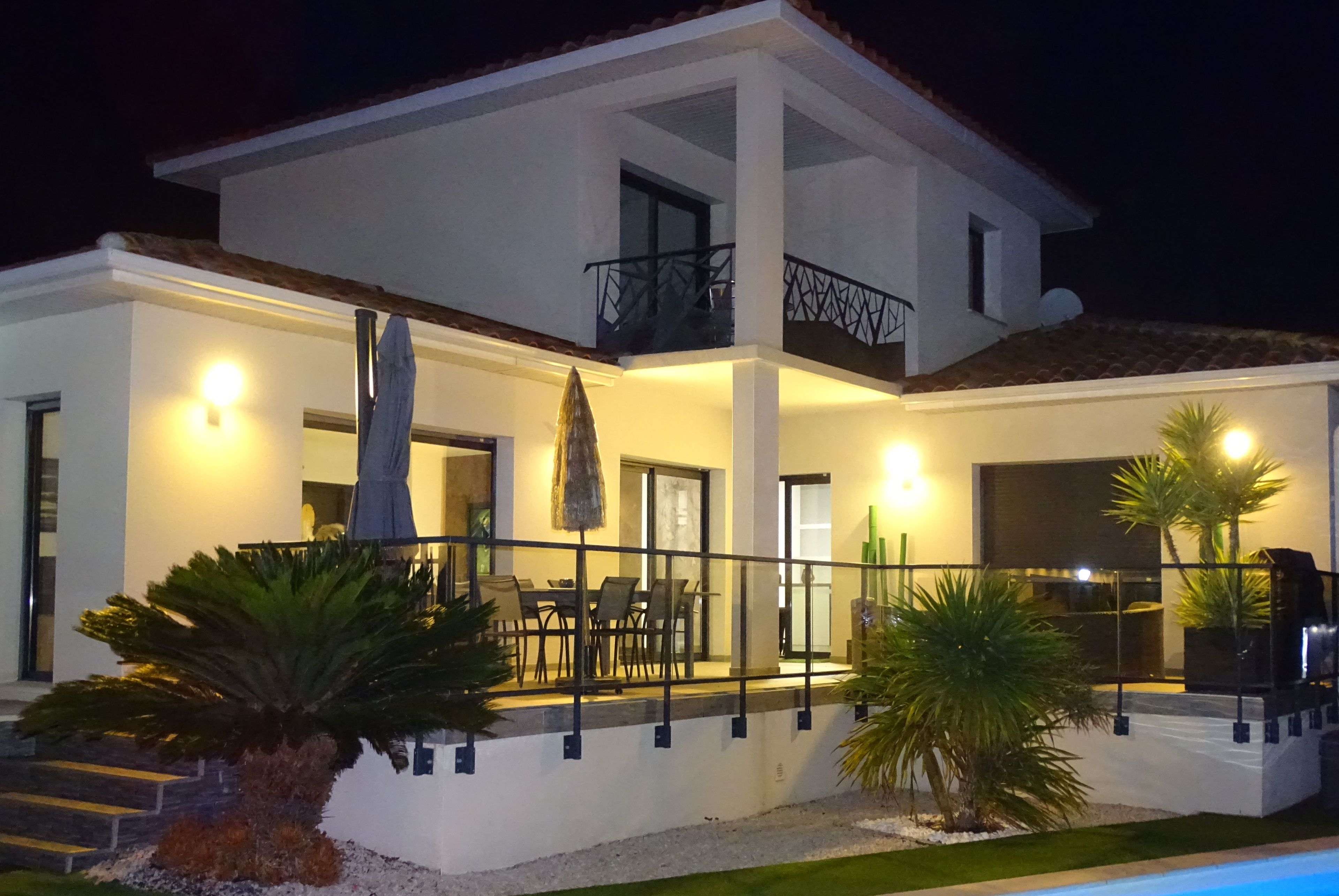 A modern two-story house with a pool, outdoor seating, and a well-lit balcony.