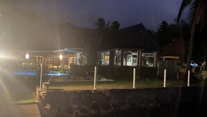 Vista nocturna de un resort con piscina, mobiliario exterior y un edificio bien iluminado.