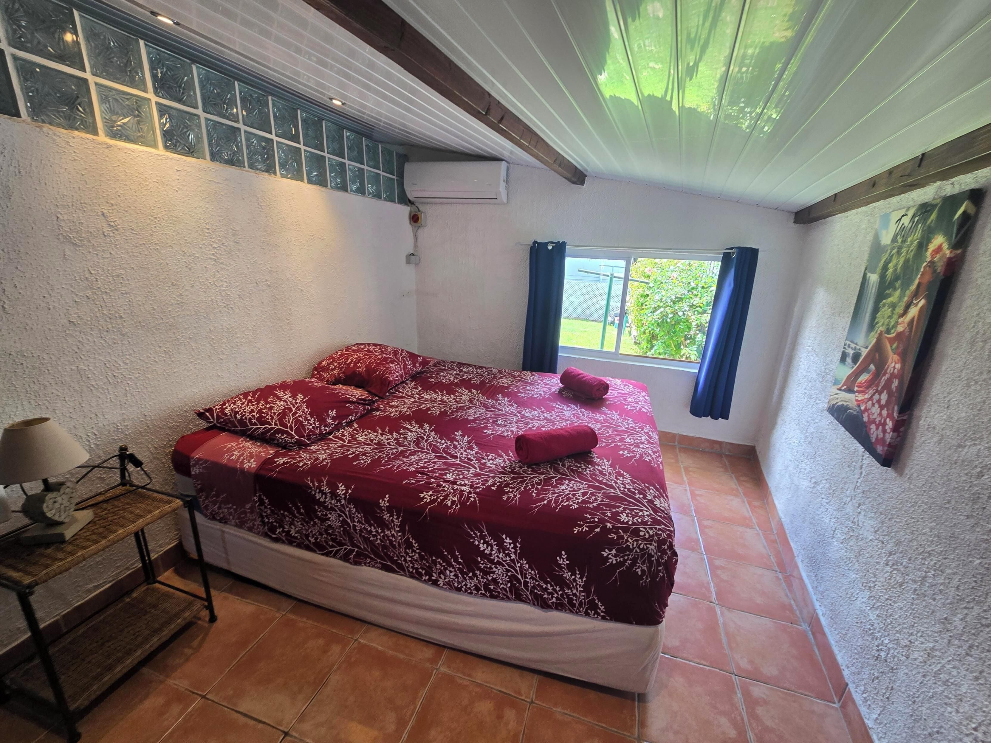 Une chambre à coucher avec un lit, une table de chevet, une fenêtre avec des rideaux et un tableau au mur.