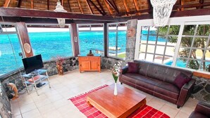 A spacious living area with a large window overlooking the ocean, a wooden coffee table, a sofa, and a TV on a stand.