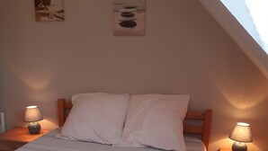 Un dormitorio con una cama, dos mesitas de noche con lámparas y dos cuadros colgados en la pared.