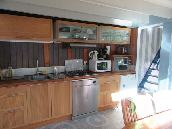 A compact kitchen with wooden cabinets, a stainless steel dishwasher, a gas stove, a microwave, and a coffee maker.