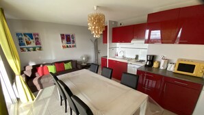 A modern kitchen with red cabinets, a dining table with chairs, and a small kitchenette area. - SERIGNAN - Apartment for 4 people with air conditioning (Sérignan)