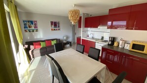 A compact living space with a dining area, kitchenette, and a sofa with colorful cushions. - SERIGNAN - Apartment for 4 people with air conditioning (Sérignan)