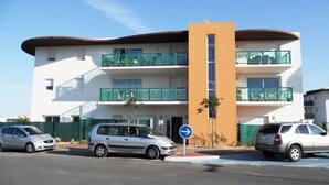 A modern multi-story building with balconies, a parking area, and a blue directional sign. - SERIGNAN - Apartment for 4 people with air conditioning (Sérignan)
