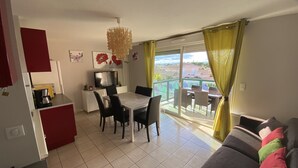 A dining area with a table and chairs, a television, and a kitchen area with a coffee machine. - SERIGNAN - Apartment for 4 people with air conditioning (Sérignan)