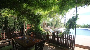 Une terrasse extérieure avec une table et des chaises en bois, entourée d’une clôture en bois et d’une végétation luxuriante.