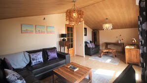 Un salon avec un plafond en bois, un canapé en cuir noir, une table basse en bois et un lustre.