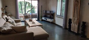 Un salon comprenant un canapé, une table basse, un téléviseur et une grande fenêtre donnant sur les arbres.