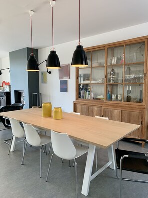 Un comedor moderno con una mesa de madera, sillas blancas y lámparas colgantes negras.