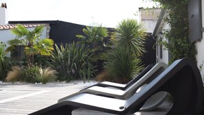 A modern outdoor lounge area with two lounge chairs and a wooden deck.