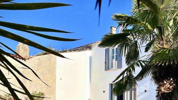 A modern pool area with a clear blue sky, a stone wall, and a white building with a window.
