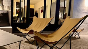 A room with two beige lounge chairs, a wooden floor, and a large window with dark frames.