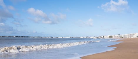Une plage avec des vagues, un ciel dégagé et des bâtiments en arrière-plan.