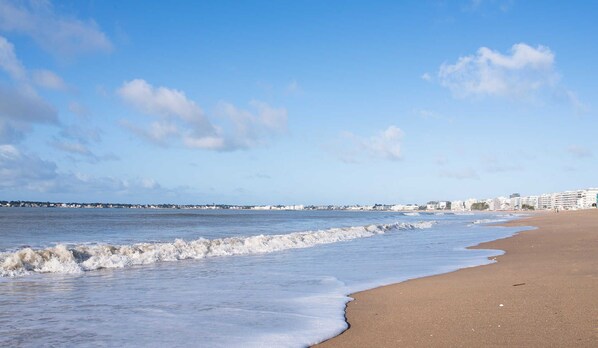 A beach with waves, a clear sky, and buildings in the background.