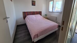 Una camera da letto con un letto, un termosifone, una finestra con tende, una porta e una parete con un quadro incorniciato.
