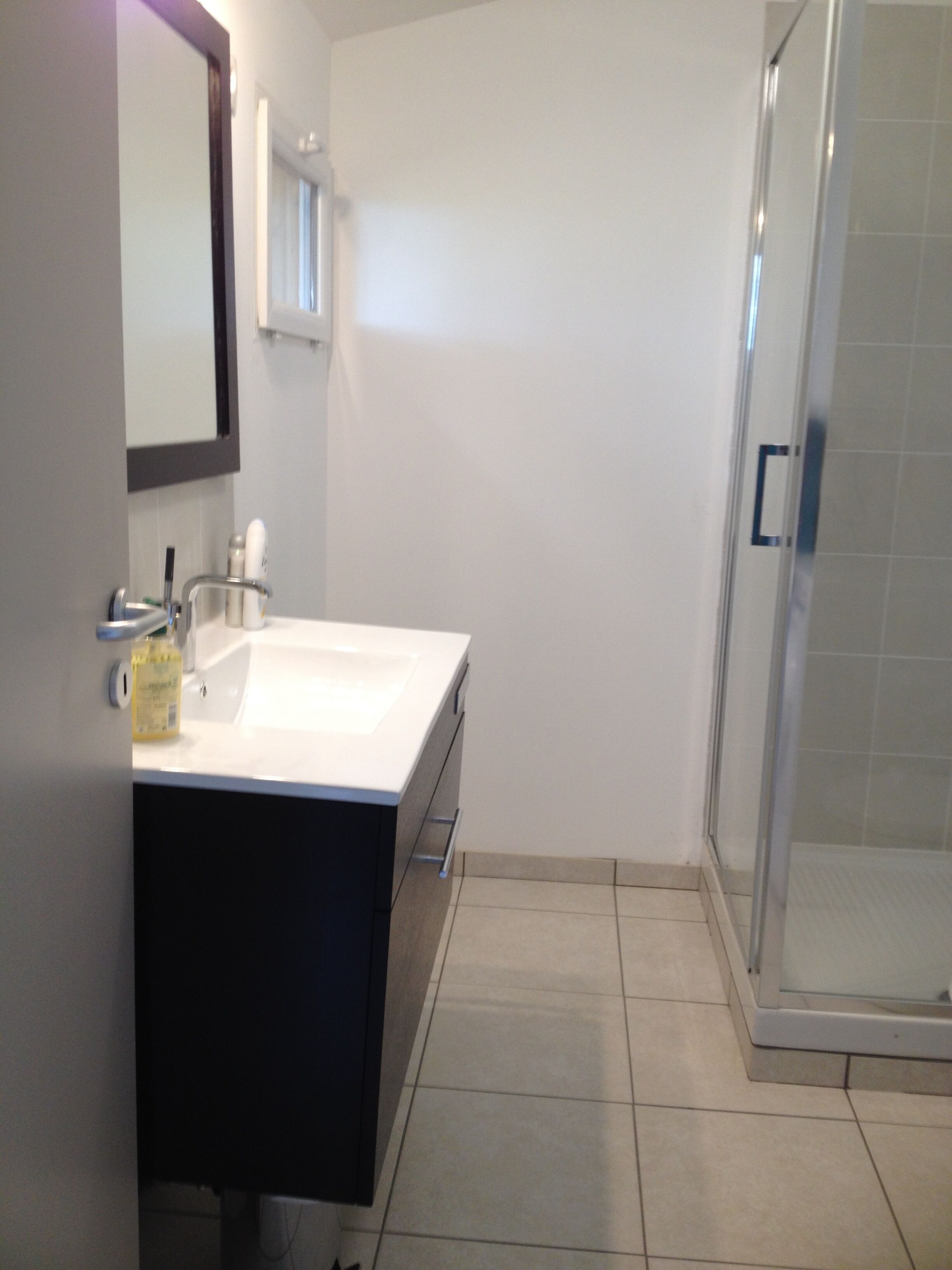 A bathroom with a white sink, dark cabinet, mirror, and a glass shower enclosure.